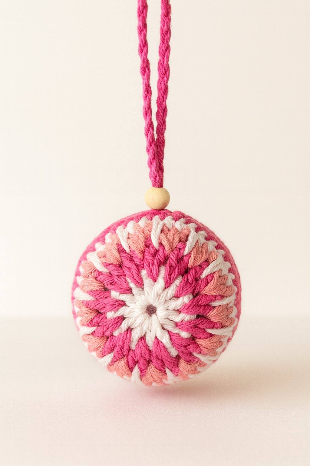 Bola Estrella de invierno Rosa – Imagen Principal del Producto Ornamento de Navidad tejido a mano en tonos rosa y blanco sobre fondo blanco, con cuerda trenzada y bolita de madera.