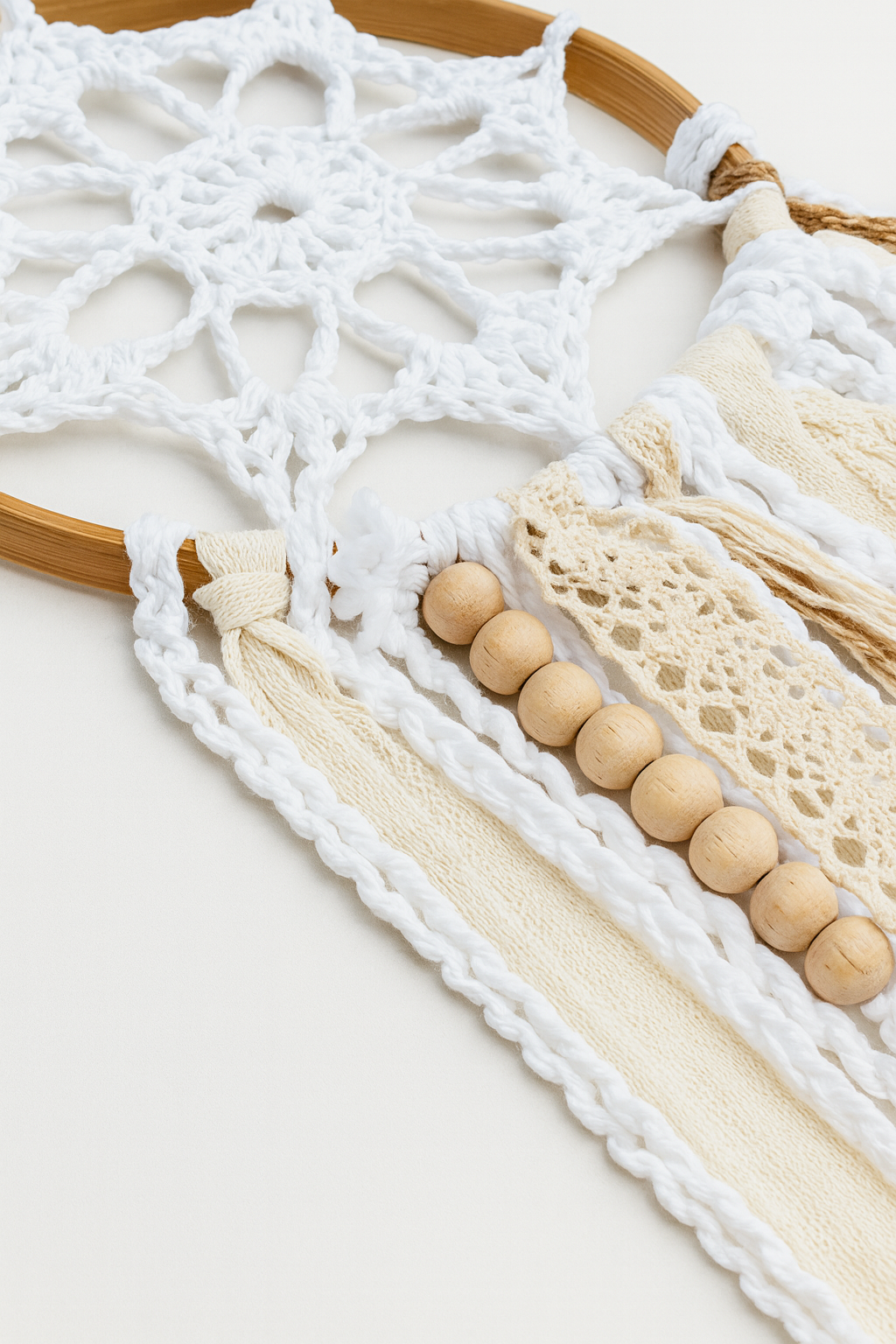 Detalle Mandala Átomo Blanco-Beige Detalle del mandala artesanal blanco y beige con crochet, cintas de encaje y cuentas de madera clara.