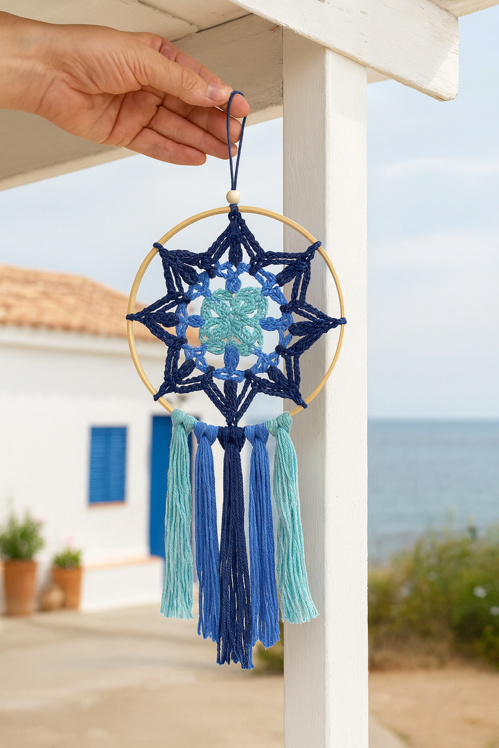 Mandala cuadrado azul – decoración artesanal en casa mediterránea Mandala cuadrado azul artesanal colgado en casa marinera blanca con detalles azules junto al mar.