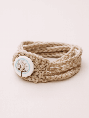 Pulsera artesanal beige de cinco cadenetas con botón de madera decorado con un árbol.