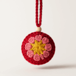 Bola Flor Rosa artesanal de crochet con detalle en madera Bola de Navidad tejida a crochet en tonos rosa, rojo y mostaza con detalle de madera, sobre fondo claro.