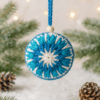 bola_estrella_invierno_crochet_contexto_claro Adorno navideño artesanal de crochet en tonos azules y blanco sobre fondo claro. Bola decorativa con forma de estrella y cuenta de madera, ideal para decoración navideña sostenible.