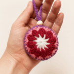 Detalle de textura de la bola flor roja Primer plano de la bola de Navidad tejida a crochet, mostrando el detalle del punto y los colores rojo, rosa y blanco con una cuenta de madera.