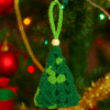 Mini Árbol de Navidad de Crochet en tonos verdes colgado en árbol decorado | Adorno artesanal sostenible – LinkArt Adorno artesanal en forma de árbol de Navidad tejido a crochet con granny square en tonos verdes y detalle de bolita de madera en imagen de contexto