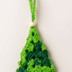 Mini Árbol de Navidad de Crochet en tonos verdes | Adorno artesanal con detalle de madera – LinkArt Adorno artesanal en forma de árbol de Navidad tejido a crochet con granny square en tonos verdes y detalle de bolita de madera, sobre fondo claro.