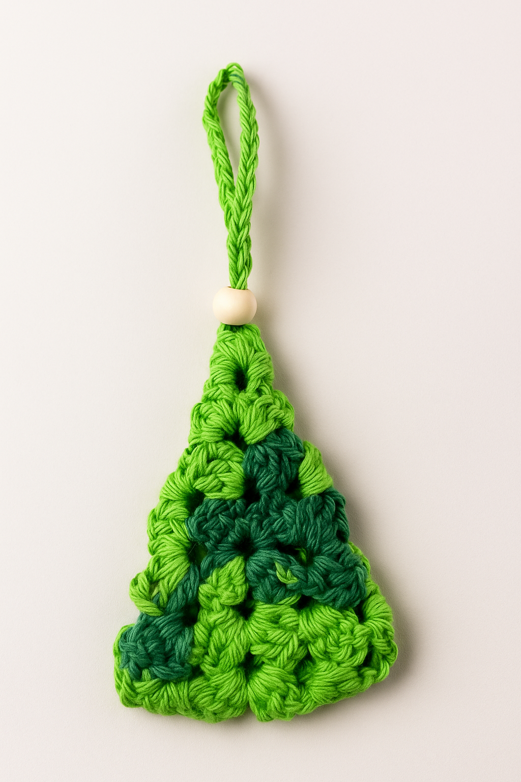 Mini Árbol de Navidad de Crochet en tonos verdes | Adorno artesanal con detalle de madera – LinkArt Adorno artesanal en forma de árbol de Navidad tejido a crochet con granny square en tonos verdes y detalle de bolita de madera, sobre fondo claro.