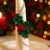 Servilletero de acebo a crochet en mesa navideña acogedora Servilletero de acebo a crochet con hojas verdes y bayas rojas en una mesa de Navidad iluminada con luces cálidas y fondo desenfocado.