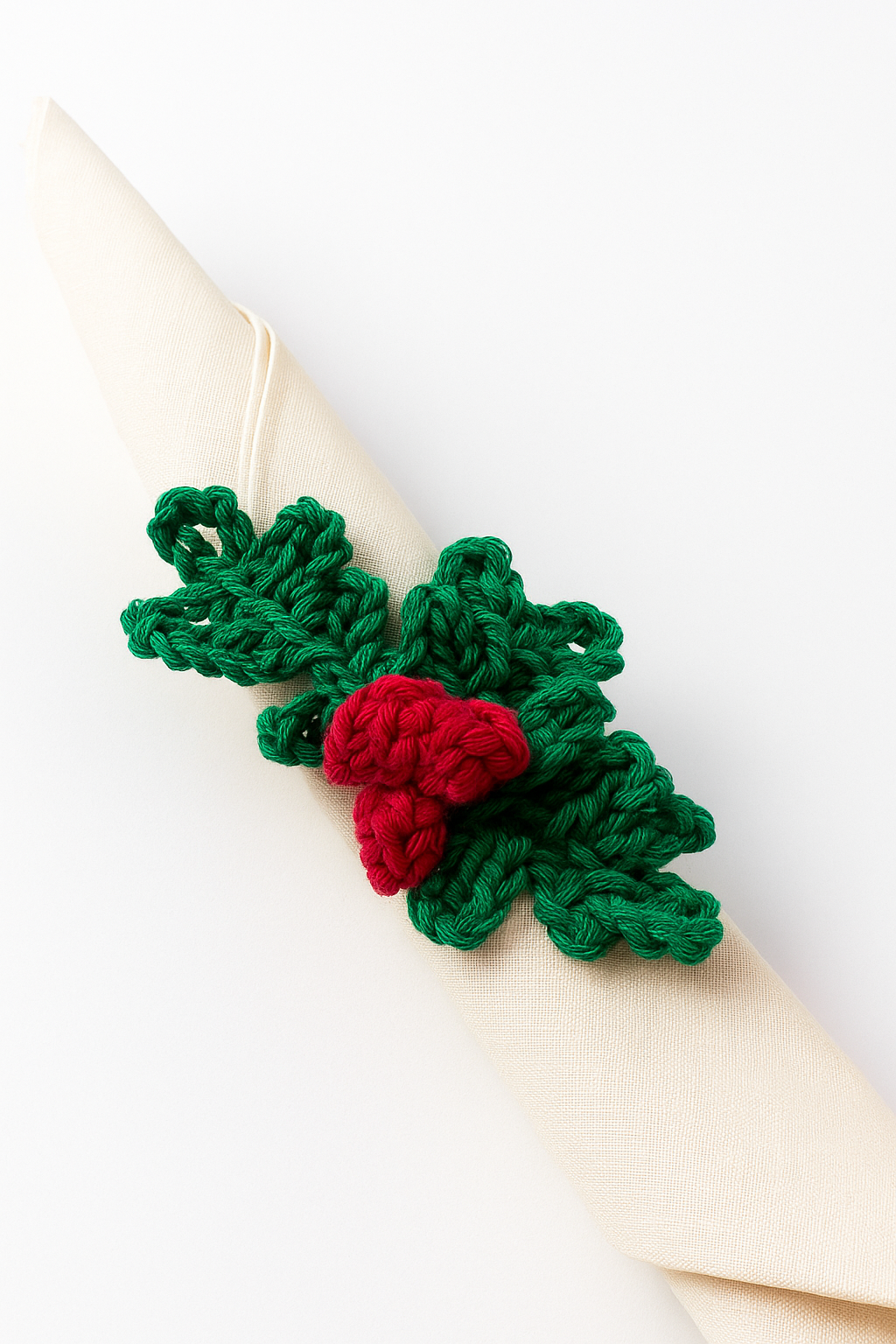 Servilletero de acebo artesanal sobre servilleta de lino Detalle del servilletero de acebo a crochet con hojas verdes y bayas rojas sobre una servilleta clara.